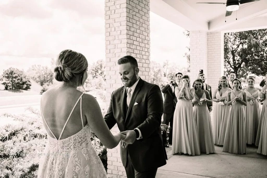 Groom looking at brides hands during first look while bridal party watches. 