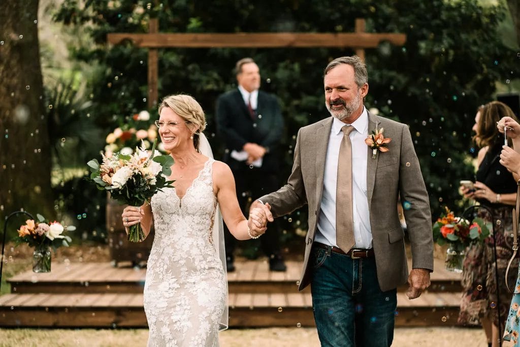 Couple walking through a aisle of champagne bubbles at their wedding ceremony, surrounded by happy guests