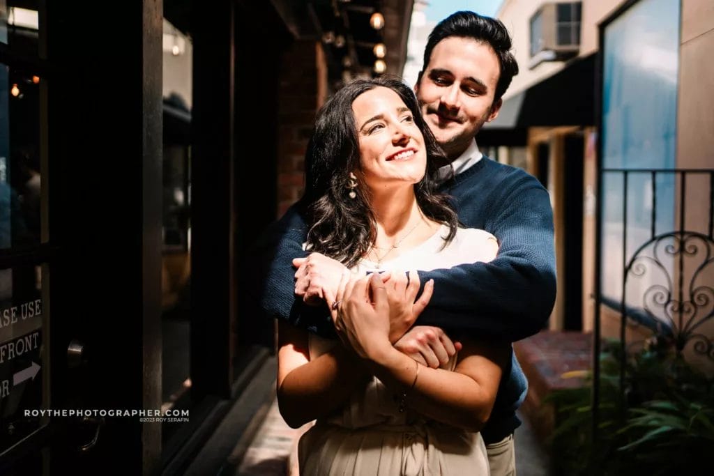 A woman with her fiance's arms around her during a winter garden engagement session