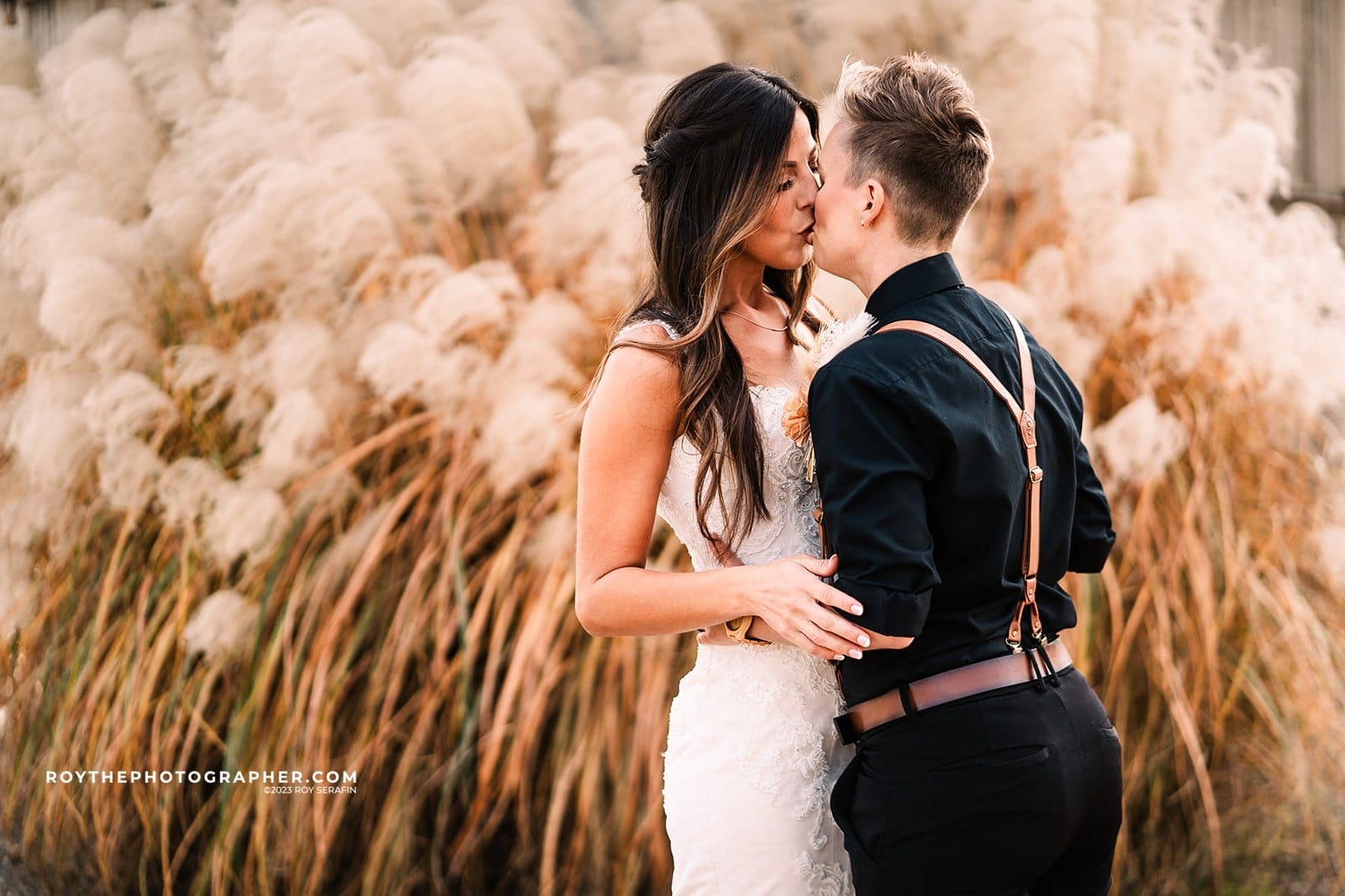Two brides kissing in front of long grass