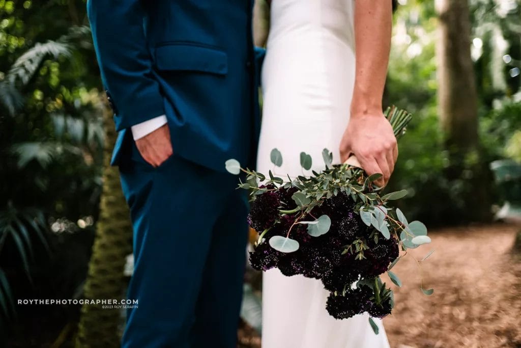 A close-up shot of a bride and groom holding hands at Sunken Gardens, with the focus on the bride's bouquet, contrasting against their wedding attire.
