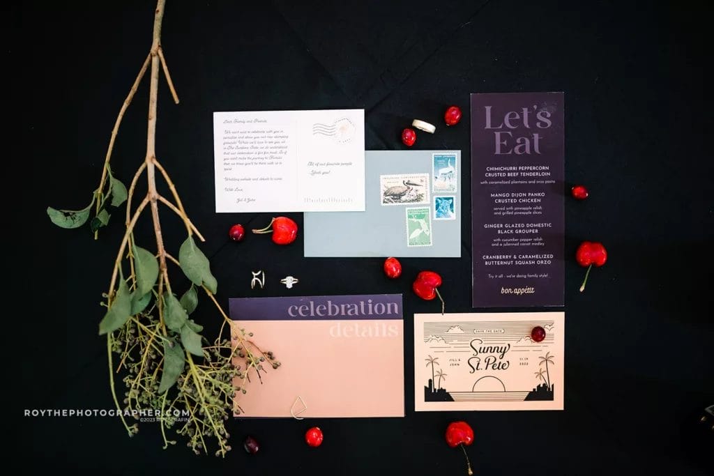 A collection of wedding stationery including invitations and menus, artfully arranged with natural elements and vibrant red accents, ready for a Sunken Gardens wedding.