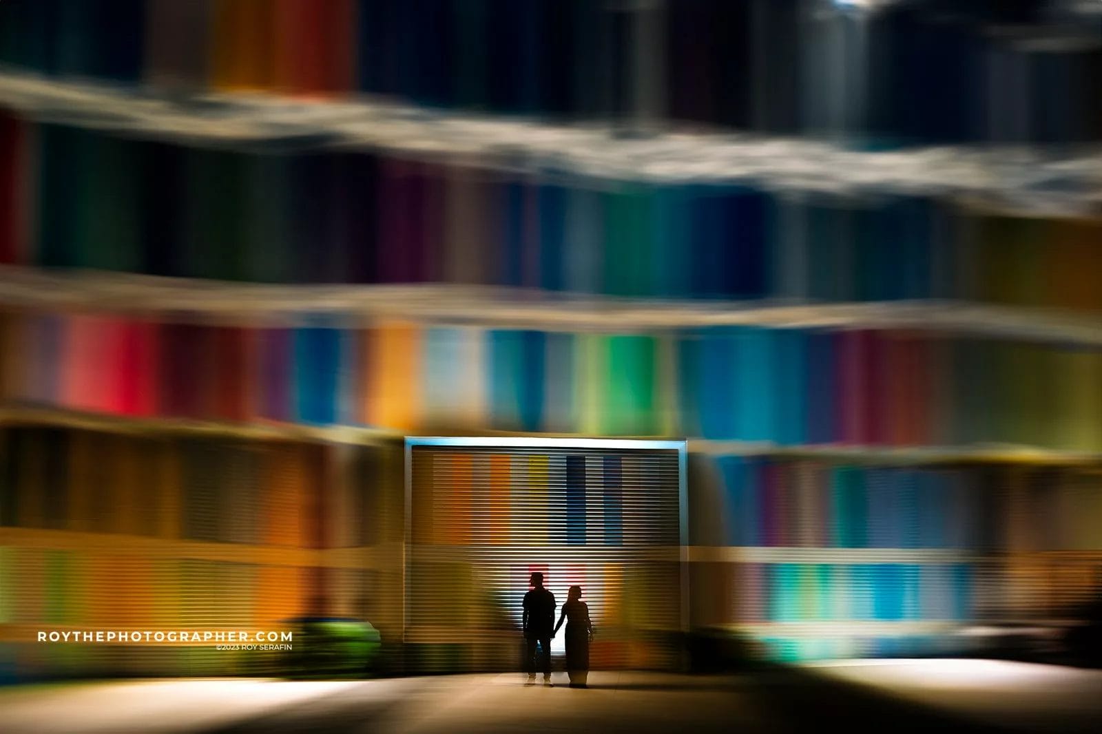 Silhouetted couple holding hands in front of a colorful abstract backdrop, featuring blurred lines of vibrant colors, creating a striking visual contrast.