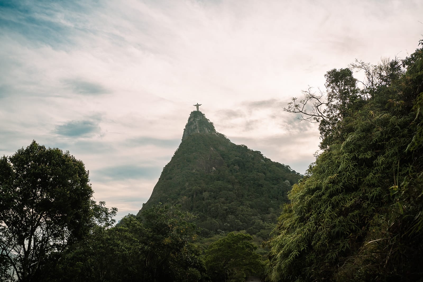 Christ the Redeemer statue atop Corcovado Mountain in Rio de Janeiro, surrounded by lush greenery and a cloudy sky.