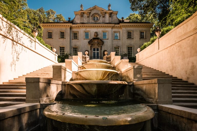 Ultimate Guide to an Atlanta History Center Wedding 1 Historic mansion with a grand staircase and cascading fountain, set against a clear blue sky and lush greenery. The architecture features classical design elements and detailed sculptures, highlighting a tranquil outdoor setting.